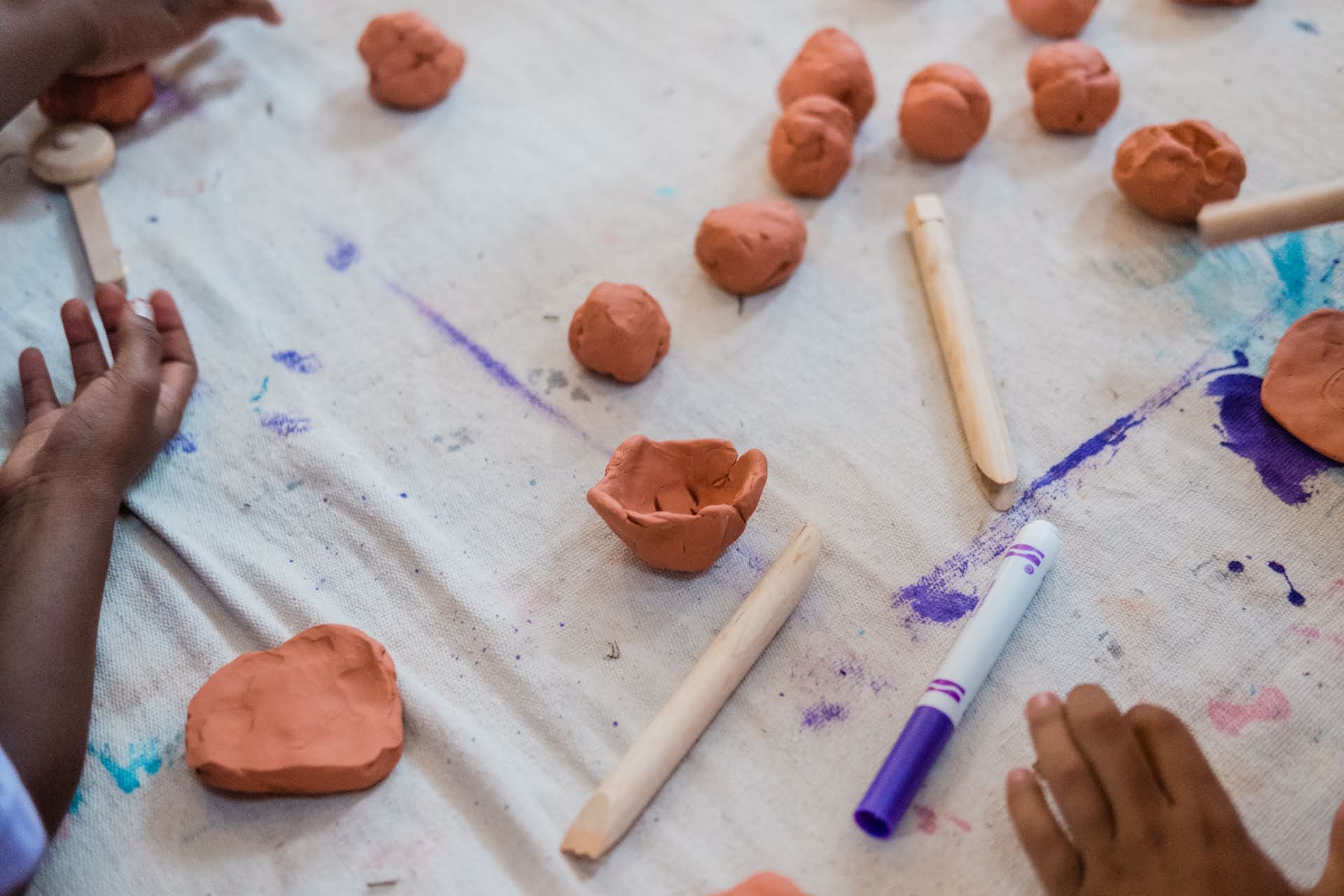 The hands of two young learners at Pittsburgh Faison K-5 school using wooden sticks and markers to shape clay.