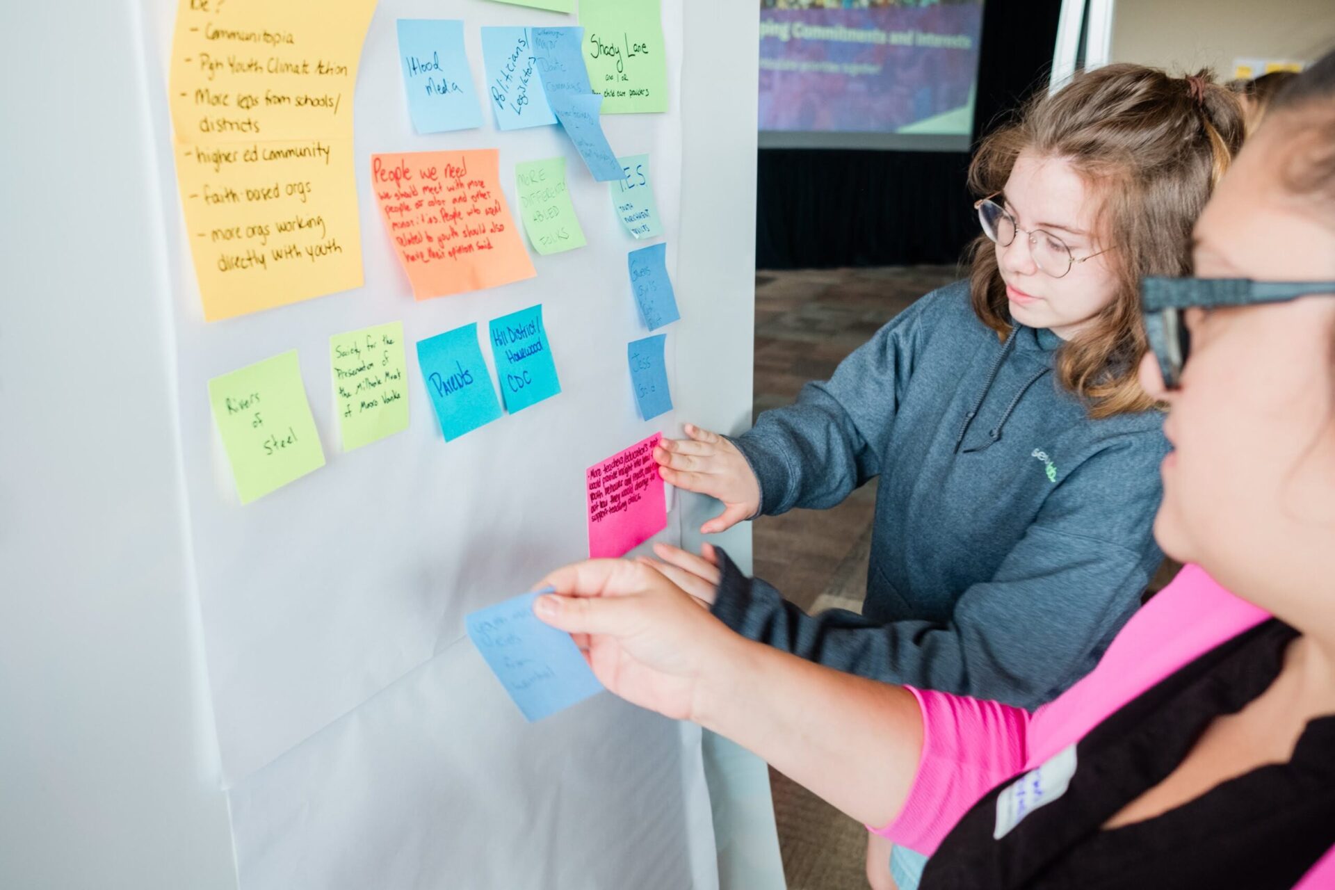 A student and an educator add post-it notes to a brainstorming sheet at a Remake Learning event.