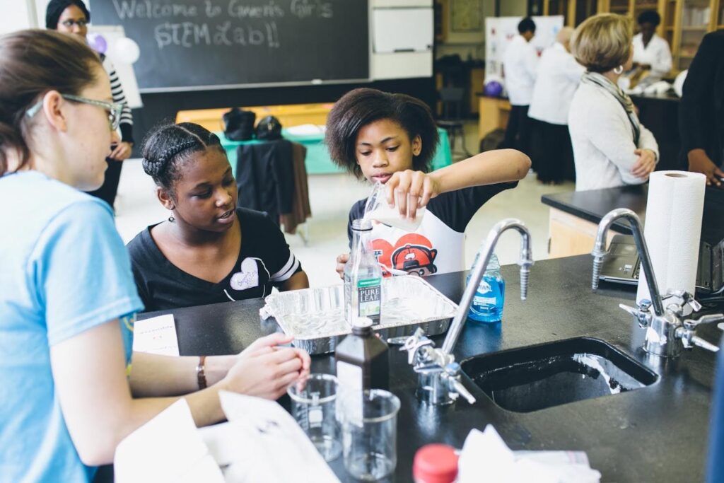 A mentor guides two girls through a science experiment.