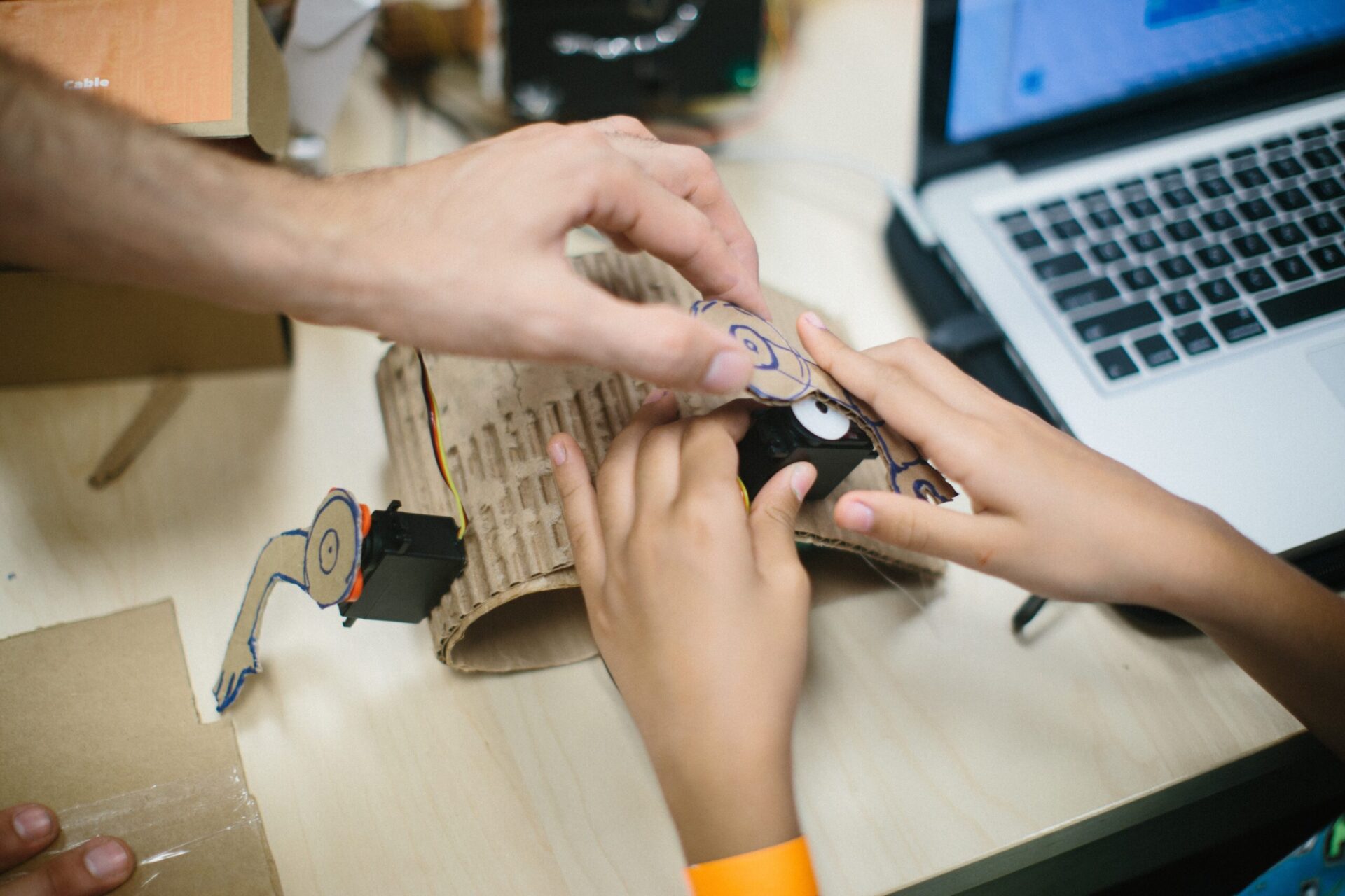 A child and an adult work together to build a robot using cardboard and a Hummingbird robotics kit.