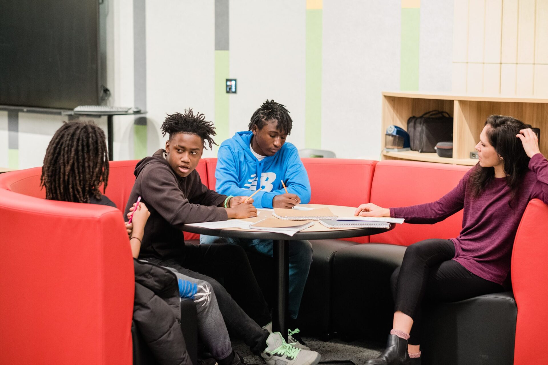 Three students and a teacher sit together at a round table in discussion.