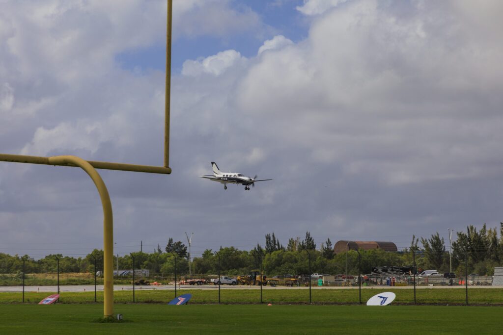 A view of a propeller plane flying above a high school football field.