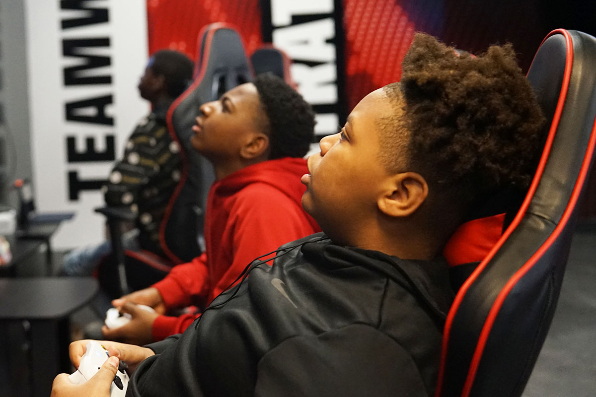 Two students recline in gaming chairs and play video games in their school's Esports arena