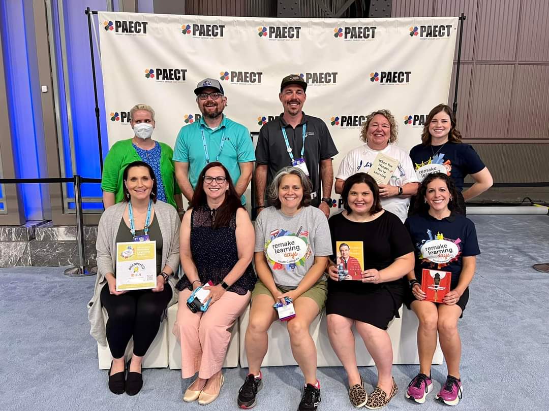 A group of people pose in front of a banner in the Remake Learning Playground area of ISTELive23.