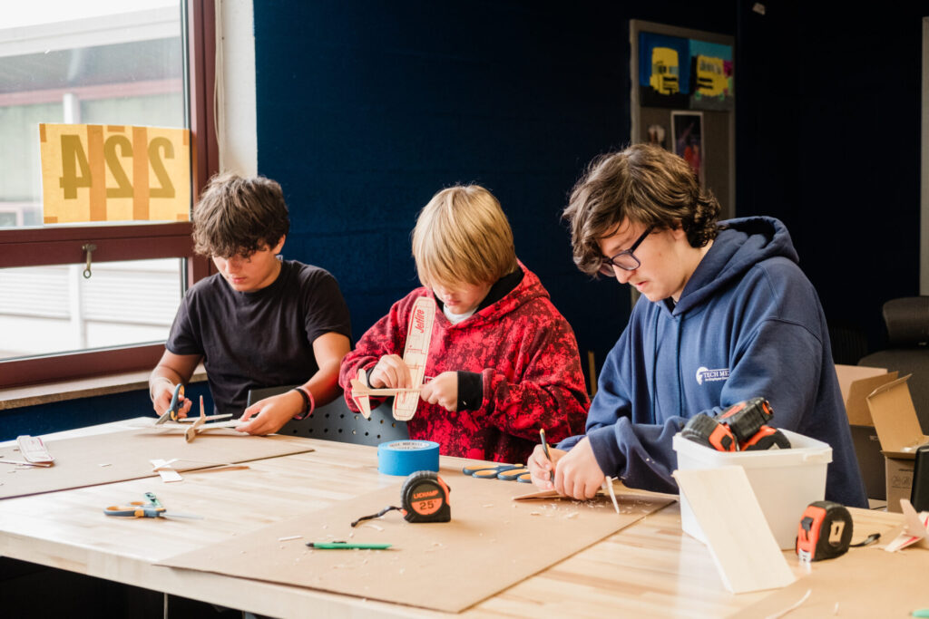 Three high school students build balsa-wood planes in aviation class.