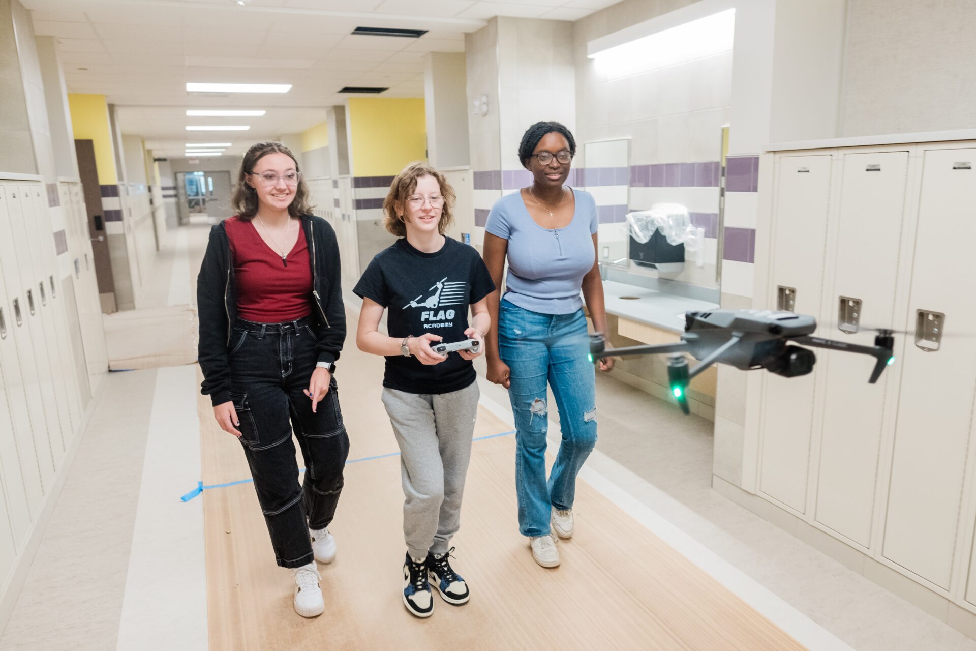 Three young women pilot a drone in a school hallway.