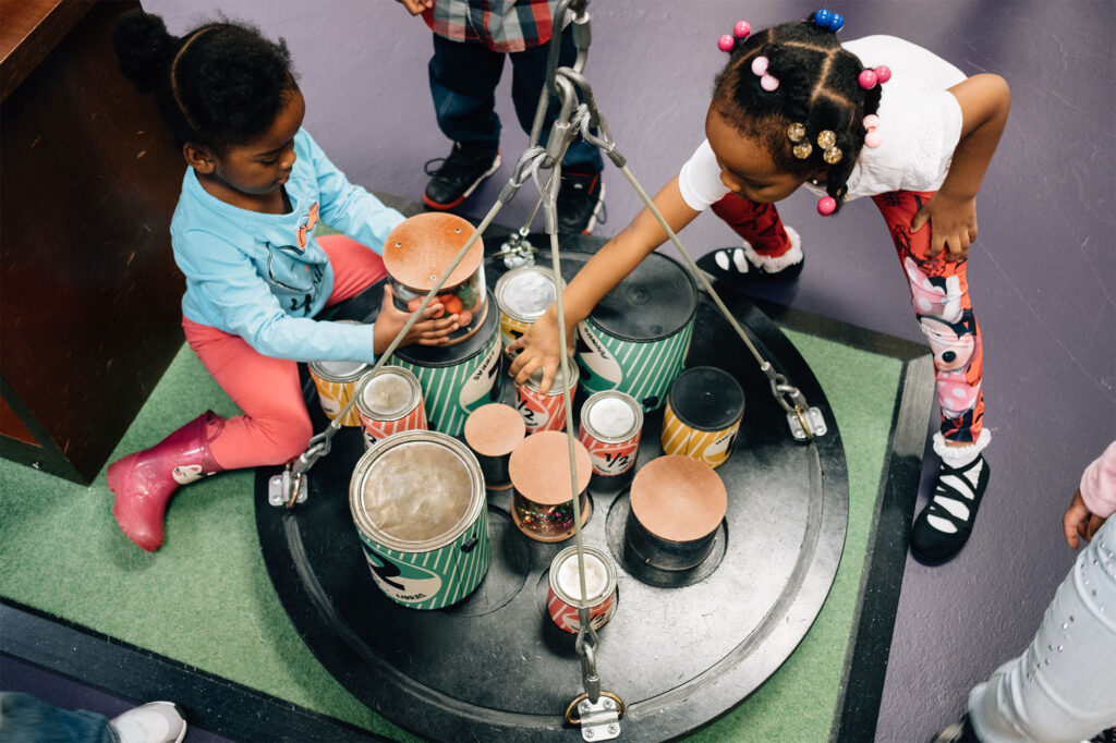 Two children playing with a big scale with several cans on it.