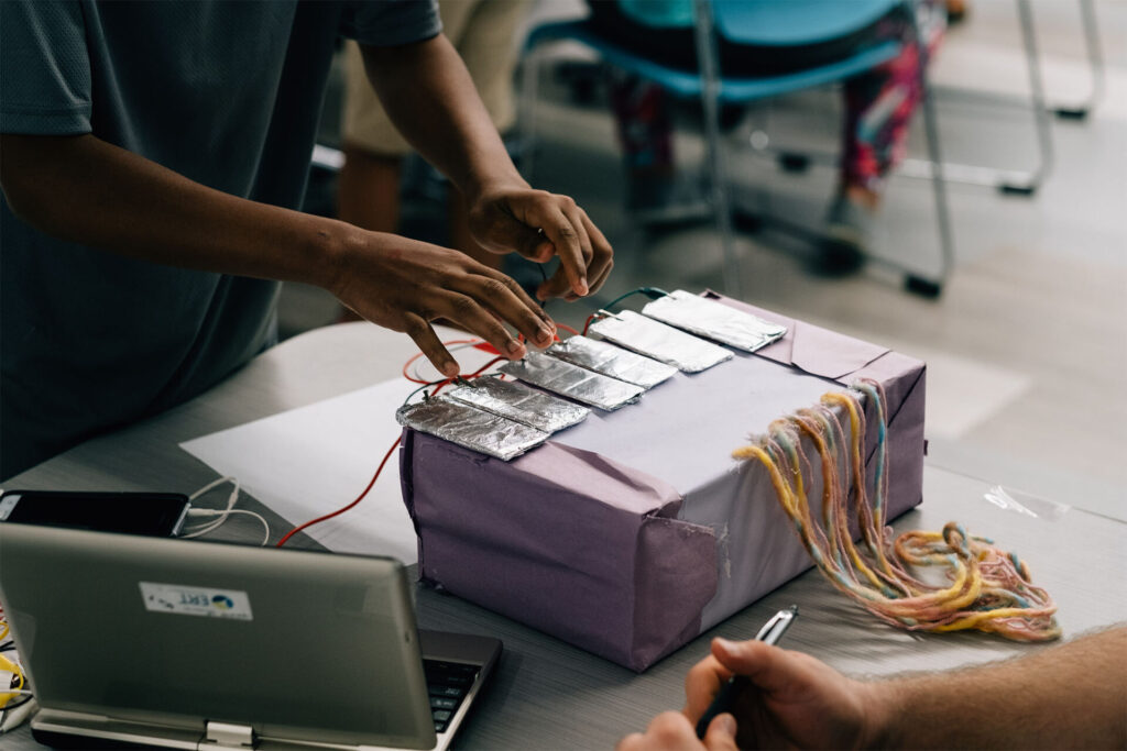 A child plays with a a box with some aluminum squares and wires coming off them.