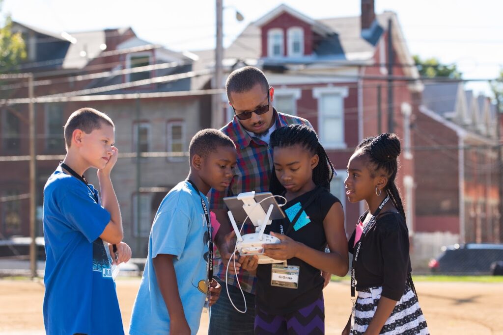 A group of children learn to fly a drone with the help of an out-of-school educator.