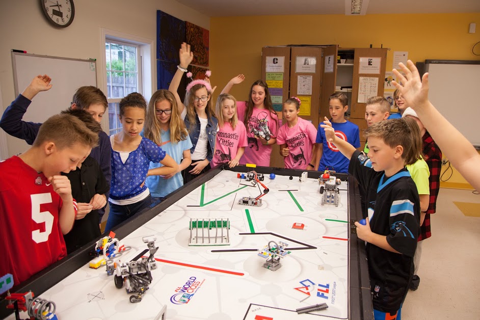 Children surrounding a table with several robots on top.