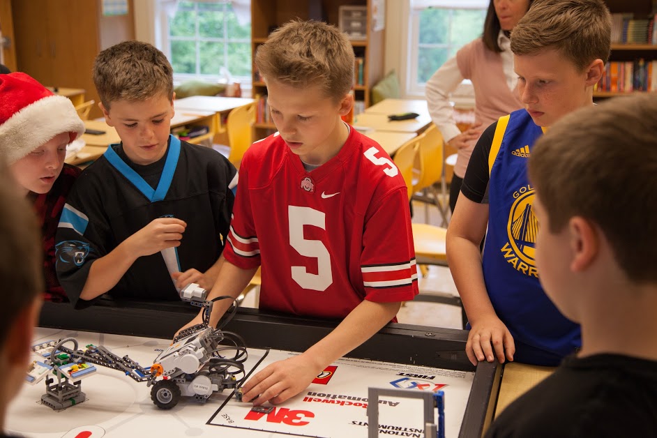 Kids surrounding a table with a robot on it.