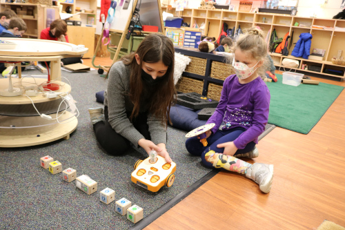 Two young girls program a robot to complete a task in their classroom.