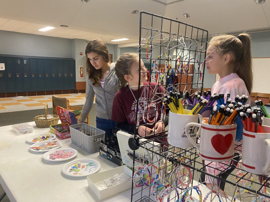Three school girls arrange items on tables in the school store.