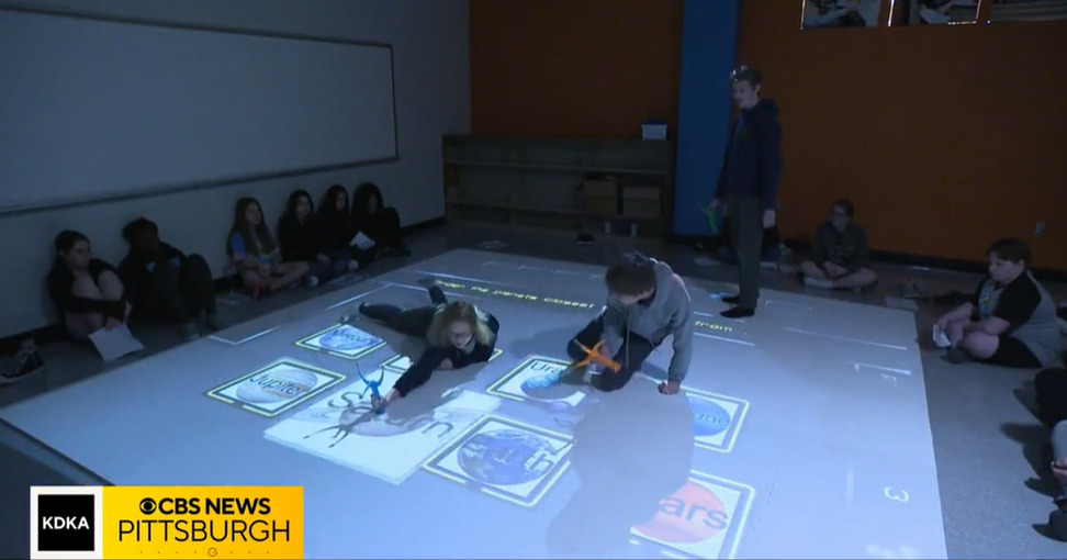 Students interact with a projected screen on the floor of a school