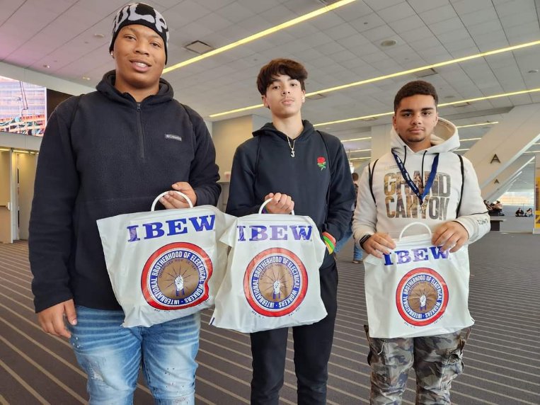 Three high school boys pose for a photo holding tote bags.