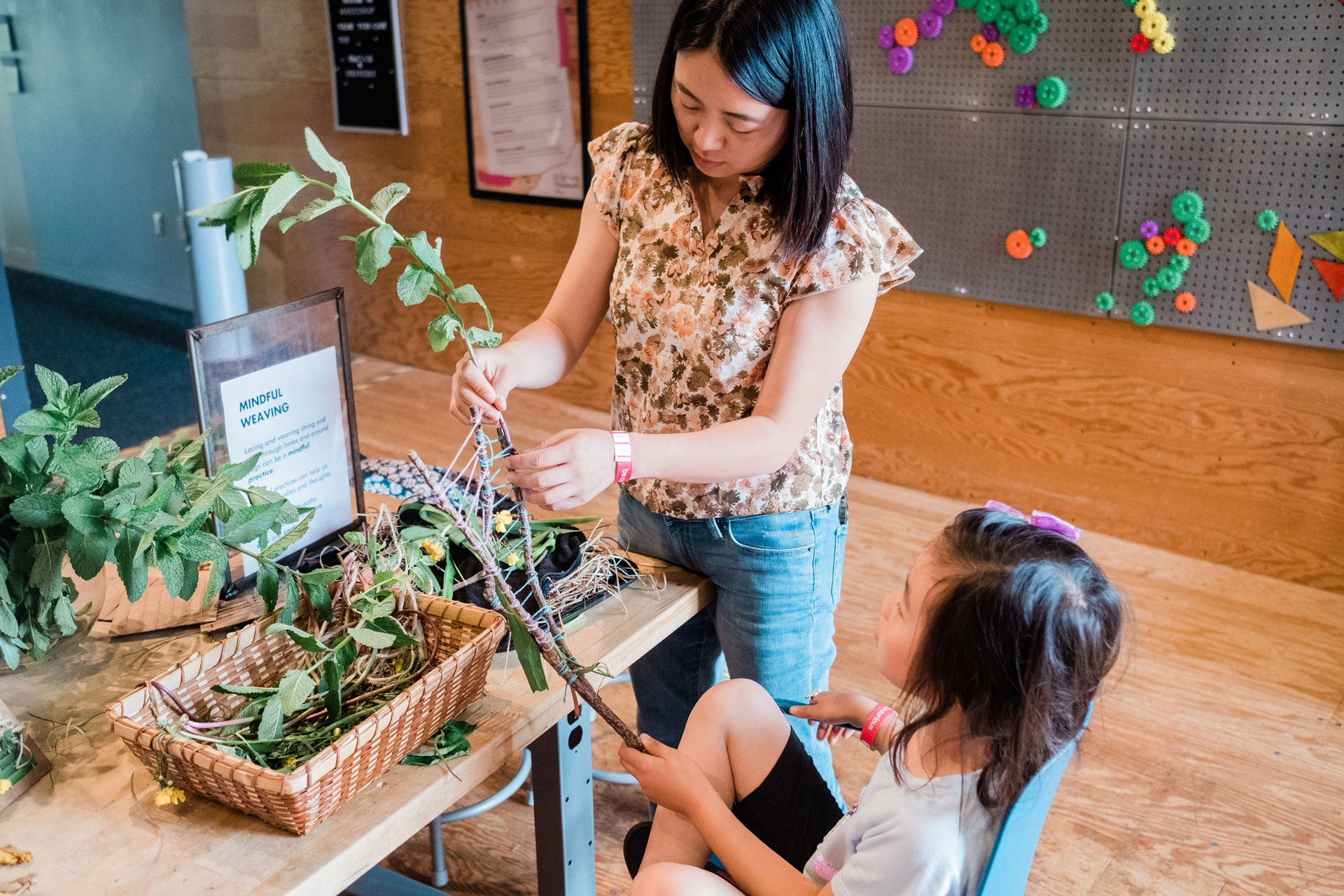 A mother and daughter weave branches and yarn in a crafting workshop.