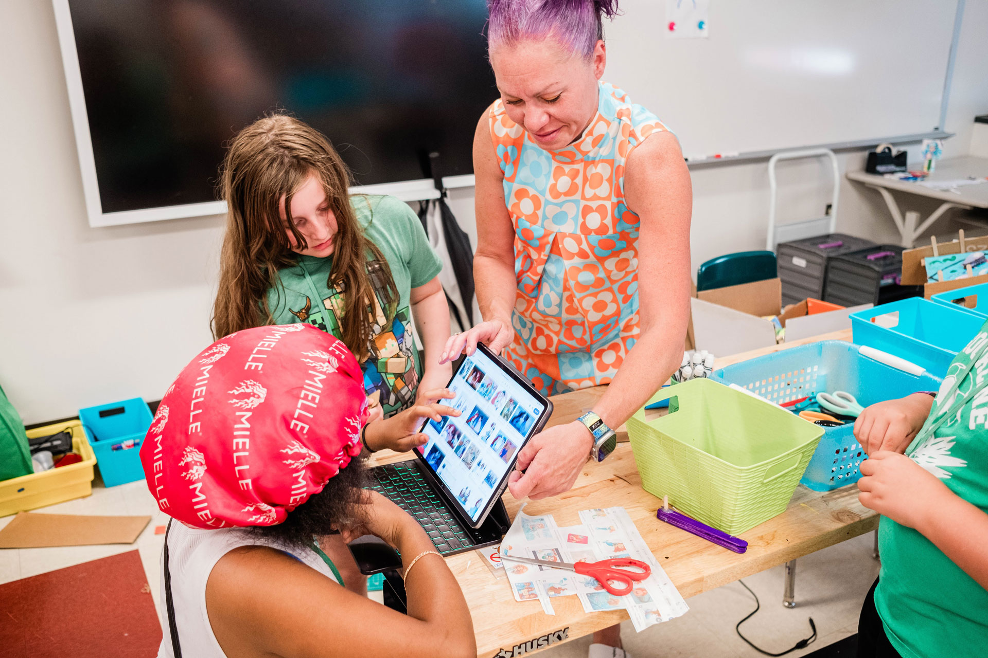 An adult shows middle school girls how to use a coding program on a touchscreen laptop.