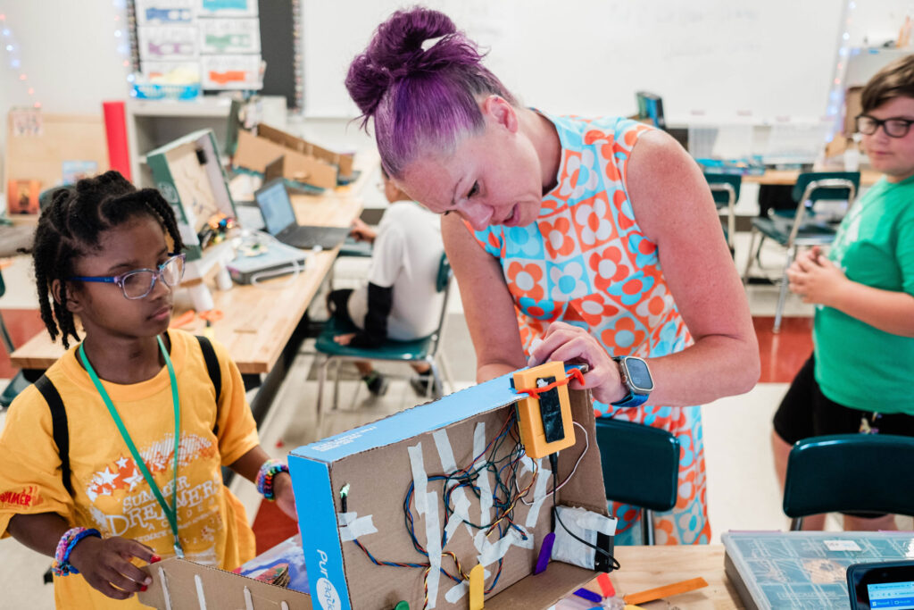 An adult educator helps a middle school student wire a do-it-yourself pinball machine.