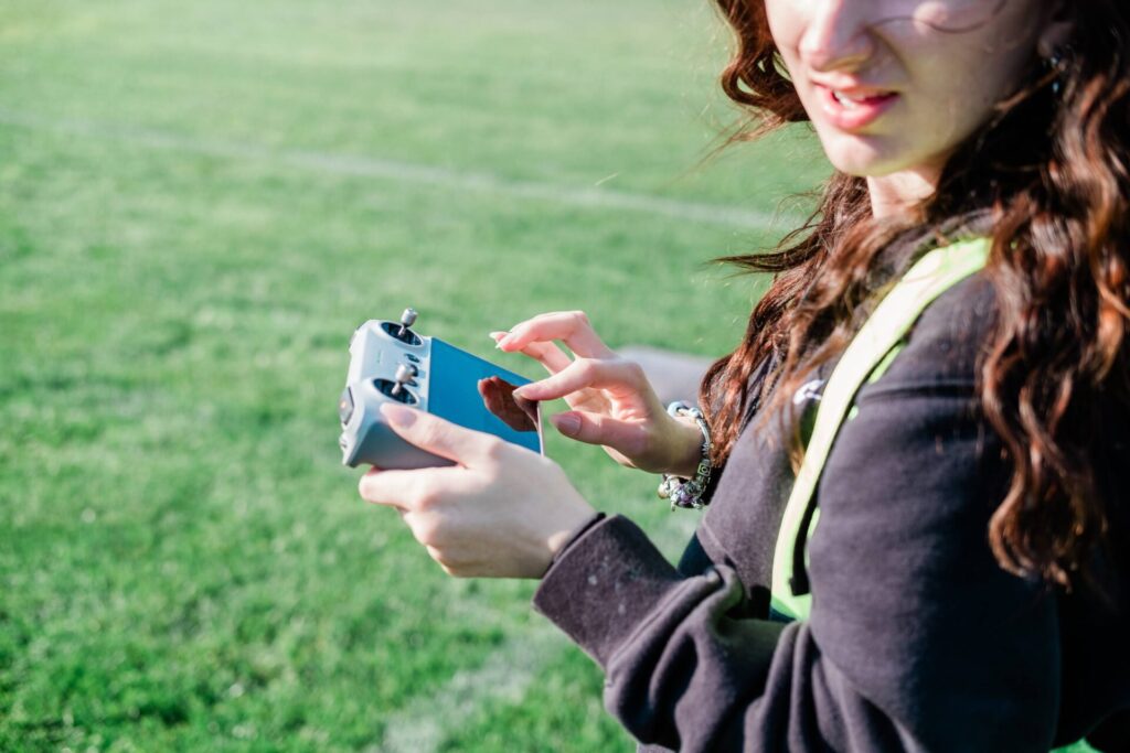 An over-the-shoulder view of a high school girl using a handheld controller to pilot a drone aircraft.