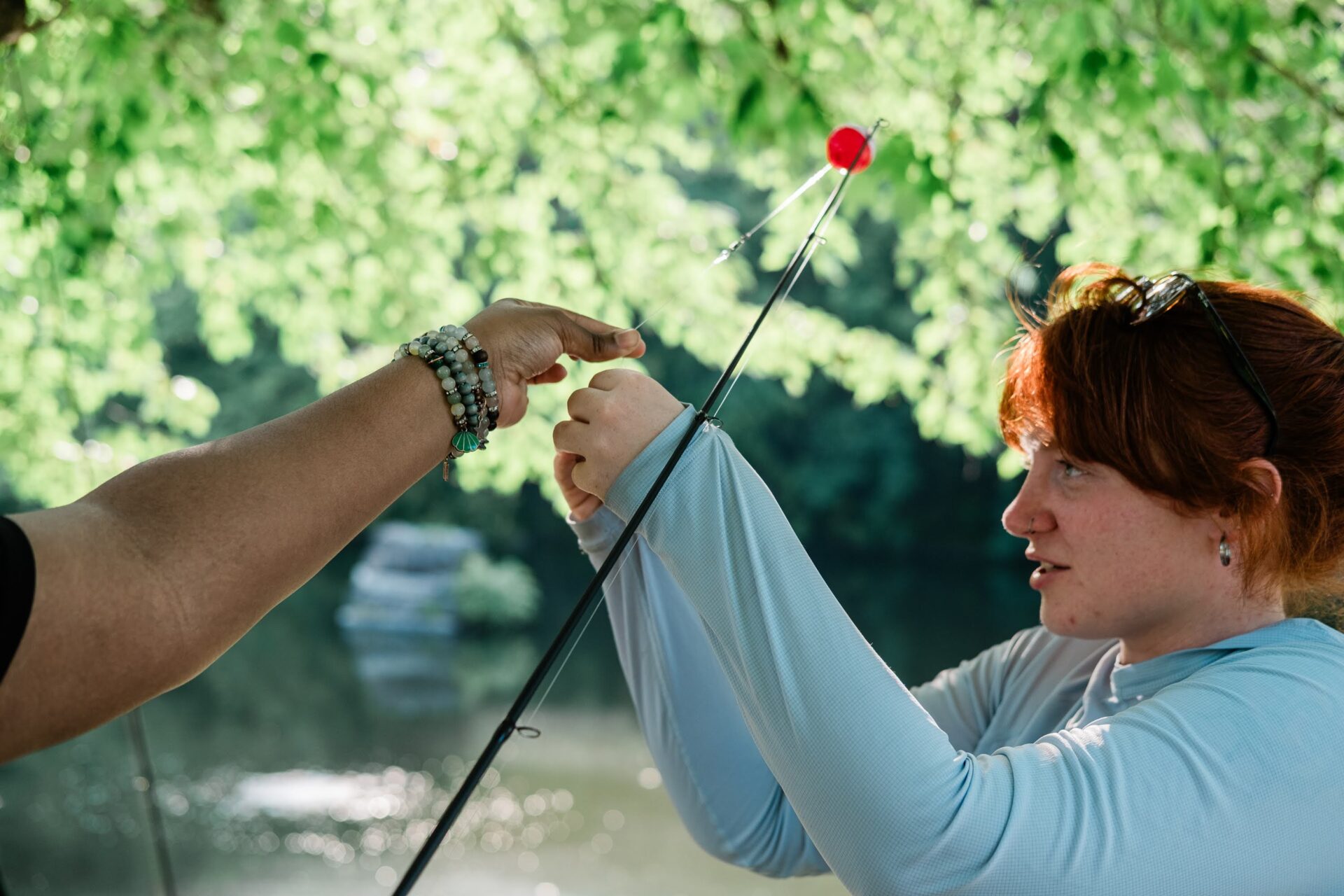 A young woman attaches a fishing lure to a fishing rod, with the help of another.