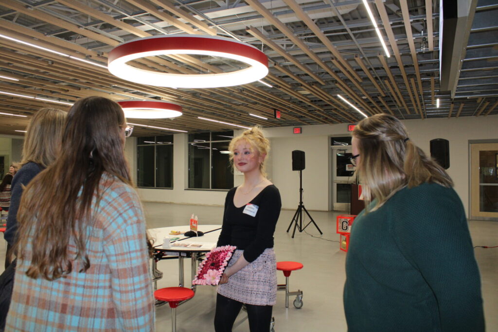 A high school aged girl speaks with a group of adults.