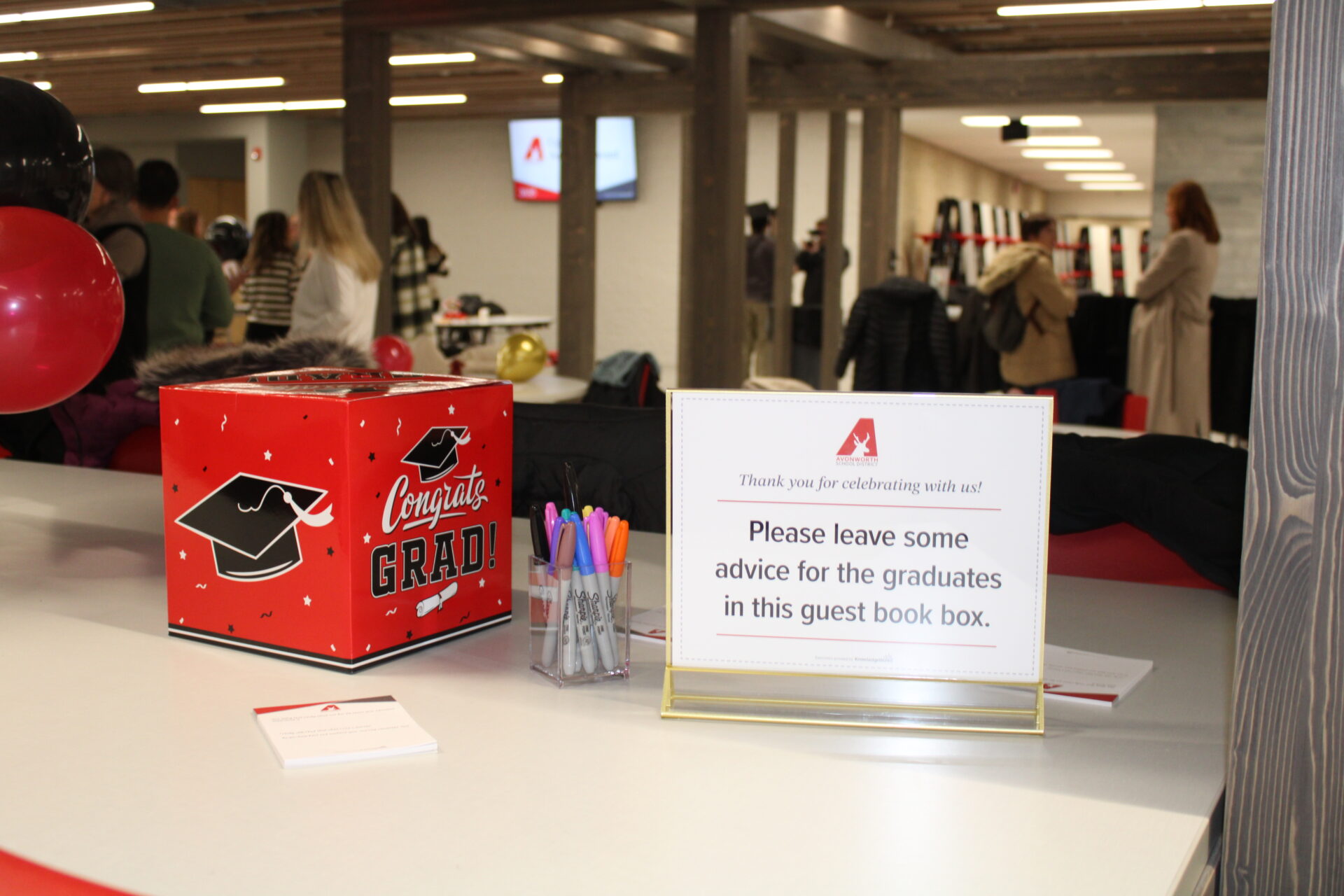 A suggestion box sits on a countertop with a sign inviting people to leave advice for high school graduates.