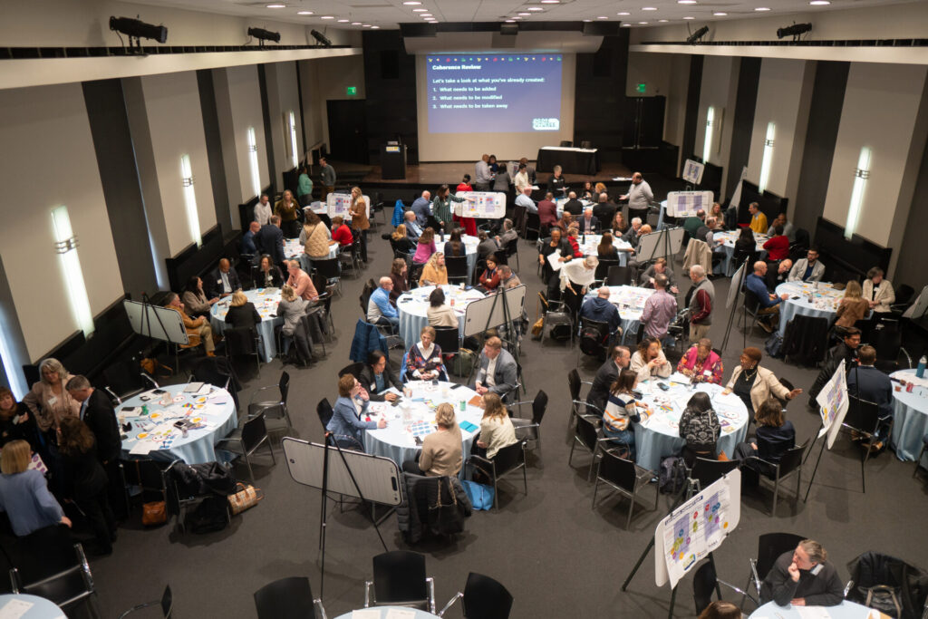 An overhead shot of a conference room filled with circular tables of people