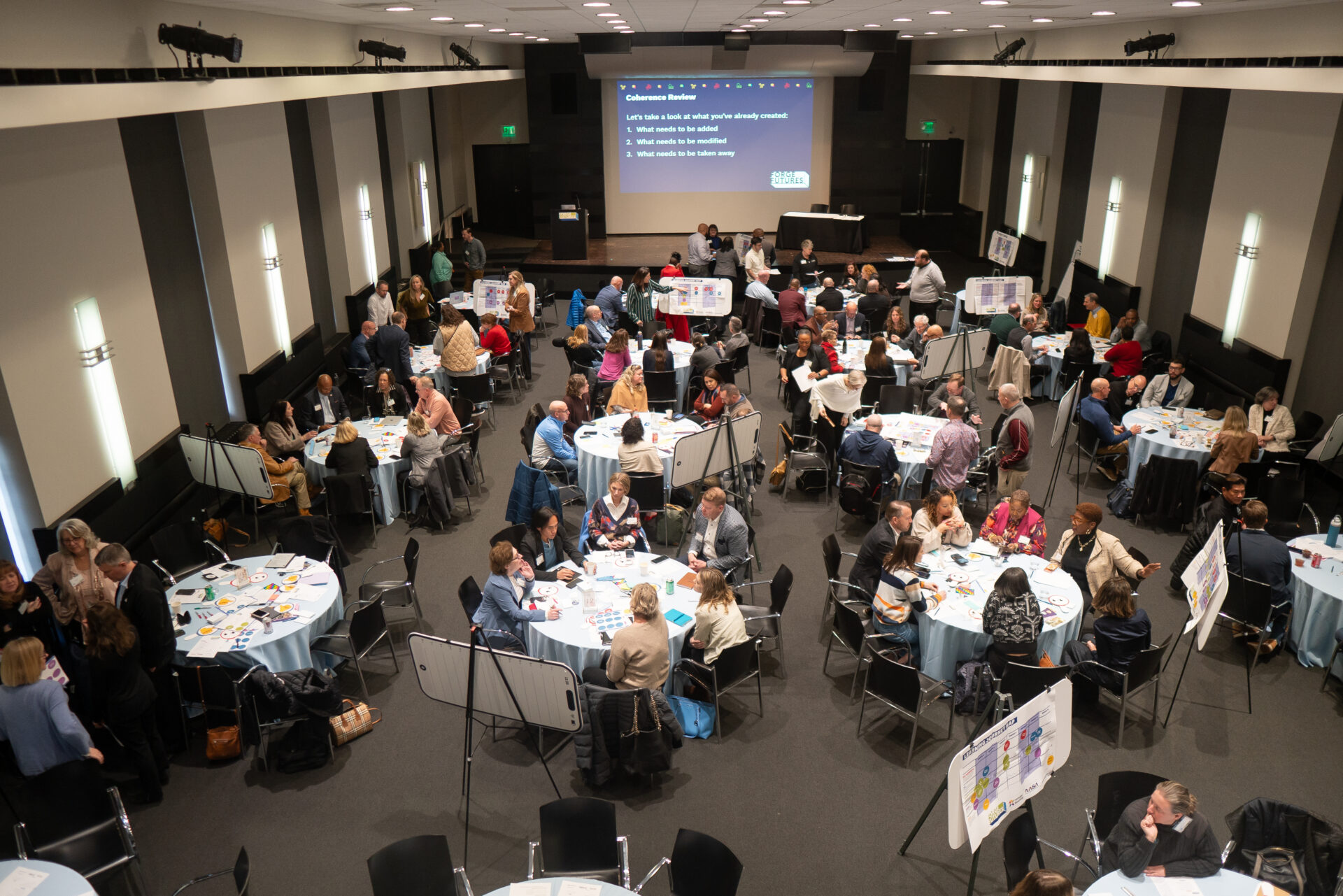 An overhead shot of a conference room filled with circular tables of people