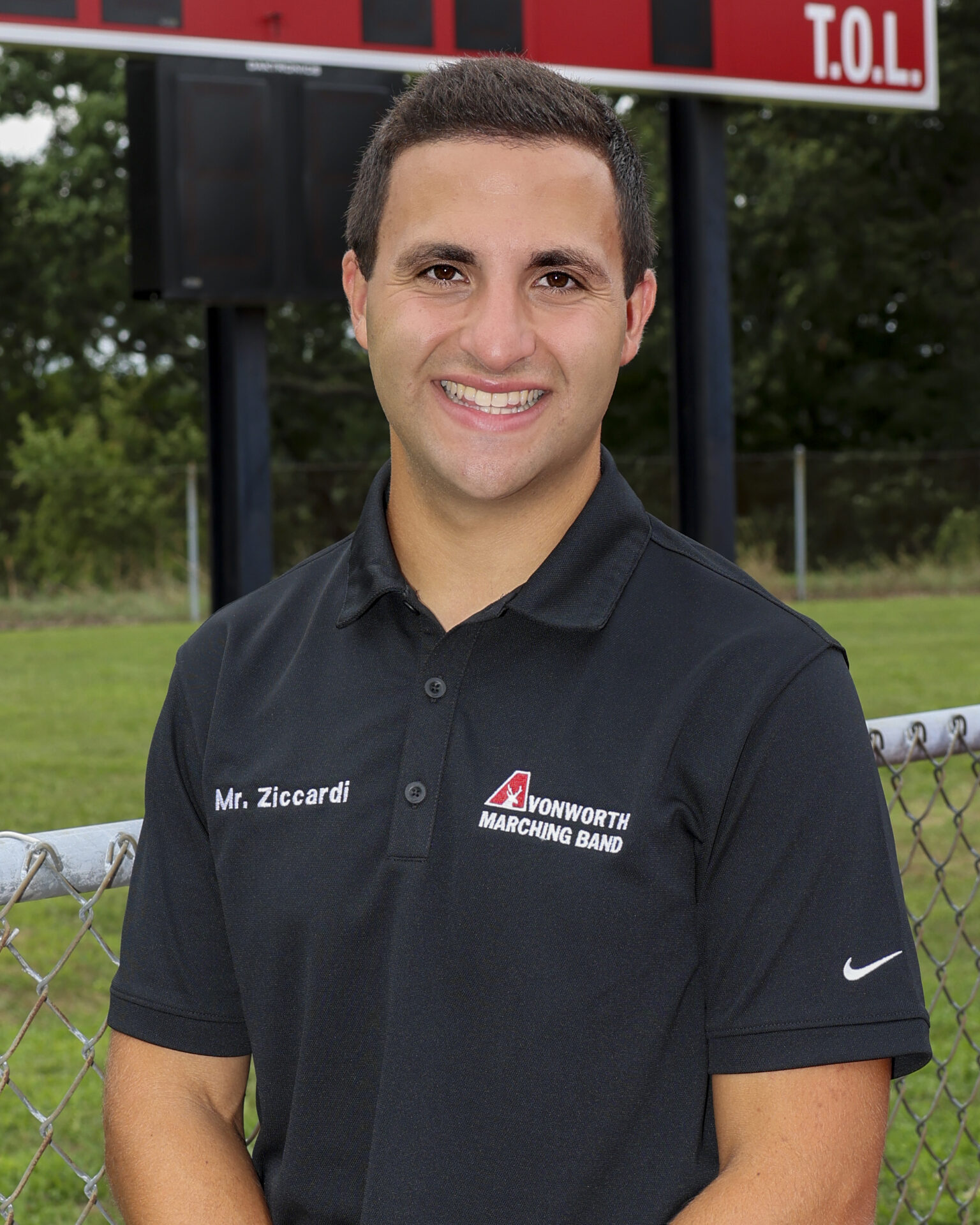 A portrait of Ronnie Ziccardi standing in front of a high school sports scoreboard.
